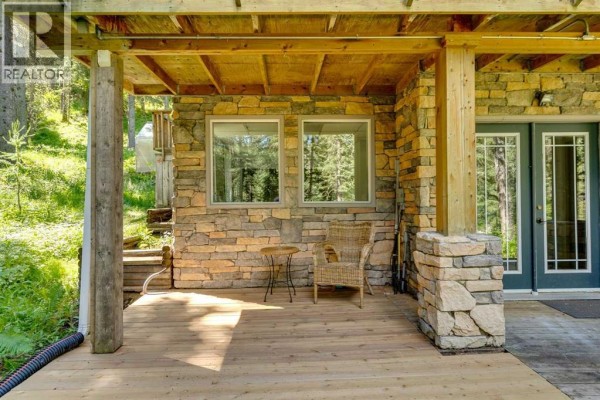 Rear exterior of a multi-story brown wood-sided house with large triangular windows and a wooden deck. - 241 Mountain Lion Drive, Bragg Creek