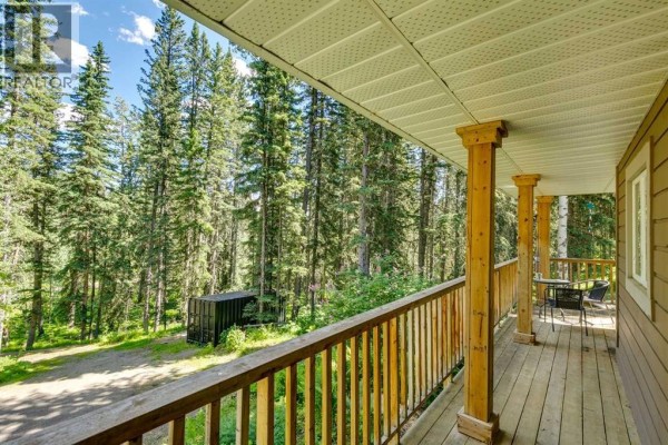 Living room with vaulted ceiling, grey sectional sofa, stone fireplace, and hardwood floors. - 241 Mountain Lion Drive, Bragg Creek