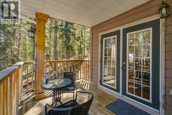 Living room with vaulted ceiling, grey sectional sofa, stone fireplace, and large windows overlooking backyard. - 241 Mountain Lion Drive, Bragg Creek