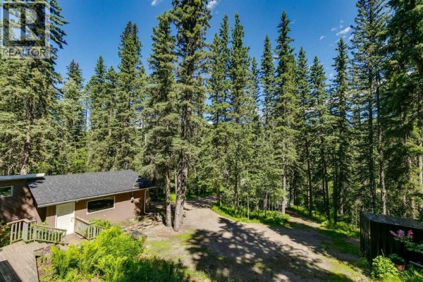 Spacious living room with vaulted ceiling, grey sectional sofa, raised dining area, and open staircase. - 241 Mountain Lion Drive, Bragg Creek