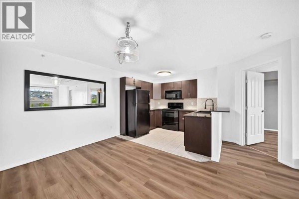 Dining area with round table, blue chairs, and view into the kitchen and hallway. - 2410, 60 Panatella Street Nw, Calgary