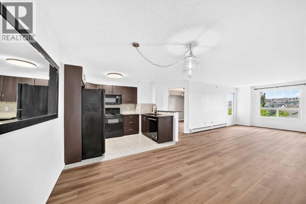 Kitchen and dining area with black appliances, light countertops, and wooden flooring. - 2410, 60 Panatella Street Nw, Calgary