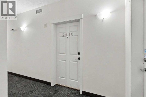 A bright hallway in an apartment building with white walls and a closed white door. - 2410, 99 Copperstone Park Se, Calgary