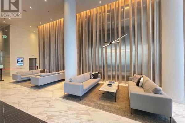 Modern apartment building lobby with grey sofas, marble floors, and a decorative metallic wall. - 2410 - 3900 Confederation Parkway, Mississauga