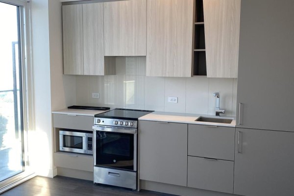 Compact apartment kitchen with light wood and grey cabinets, stainless steel appliances, and white counters. - 2410 - 3900 Confederation Parkway, Mississauga