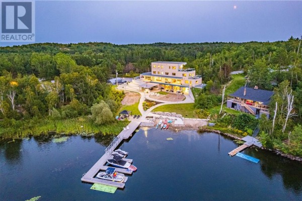 Twilight view of the property with illuminated home and dock, surrounded by forest. - 2410 South Bay Road, Sudbury