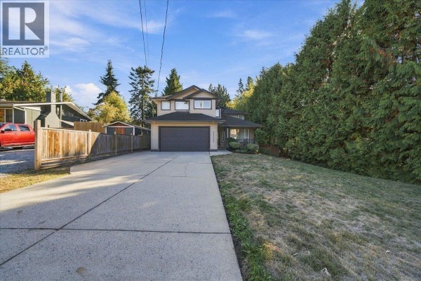 Long concrete driveway leading to a two-car garage in front of a beige two-story house. - 24100 102 Avenue, Maple Ridge