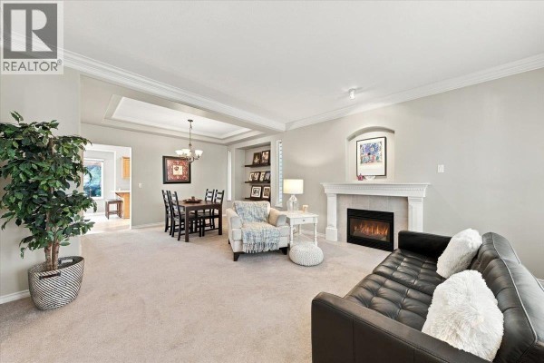 Living room with a black leather sofa, armchair, fireplace, and adjacent dining area. - 24100 102 Avenue, Maple Ridge