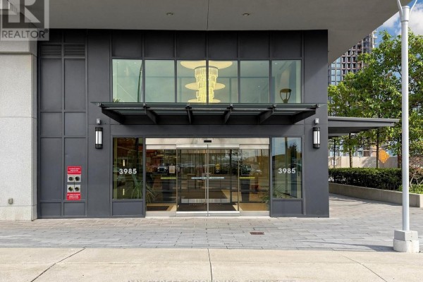 Building entrance with glass doors, dark metal facade, and pavement in front of the condominium. - 2411 - 3985 Grand Park Drive, Mississauga