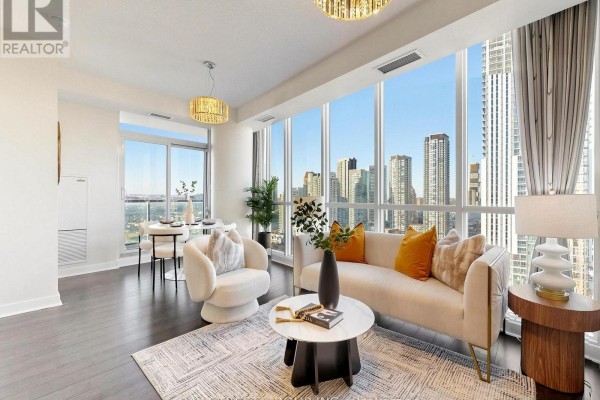 Living and dining area with large windows, city views, sofa, chairs, and dark hardwood floors. - 2411 - 3985 Grand Park Drive, Mississauga