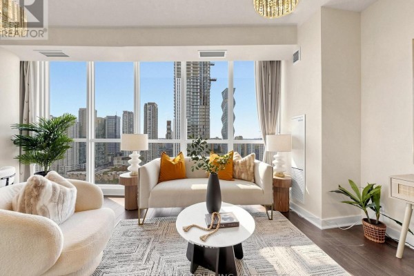 Living room with floor-to-ceiling windows offering city views, sofa, armchair, and dark wood flooring. - 2411 - 3985 Grand Park Drive, Mississauga