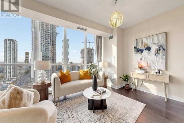 Living room with large windows overlooking the city, sofa, armchair, console table, and dark wood floors. - 2411 - 3985 Grand Park Drive, Mississauga