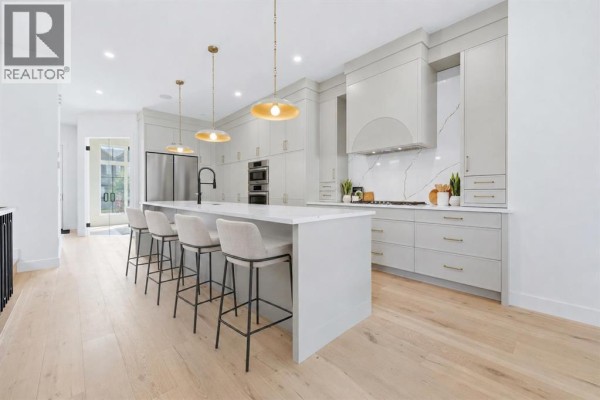 Modern kitchen with white marble countertops, gold pendant lights, and stainless steel appliances. - 2412 1 Avenue Nw, Calgary