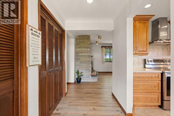 Hallway view showing wood floors, bi-fold doors, a stone fireplace, and kitchen cabinetry. - 24122 Poppe Road, Tilbury