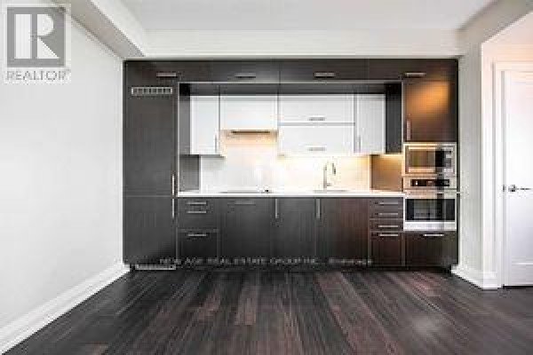 Modern kitchen with dark wood cabinets, white countertop, and stainless steel appliances. - 2419 - 5 Sheppard Avenue E, Toronto