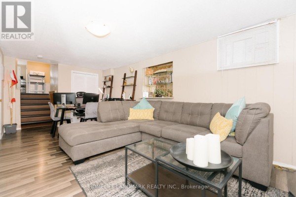 Living room with a large grey sectional sofa, glass coffee table, and a desk with computers. - 2419 Cashmere Avenue, Mississauga