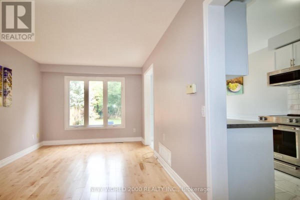 Living room with hardwood floors, lavender walls, a window overlooking the backyard, and a doorway to the kitchen. - 2419 Susquehanna Court, Oakville