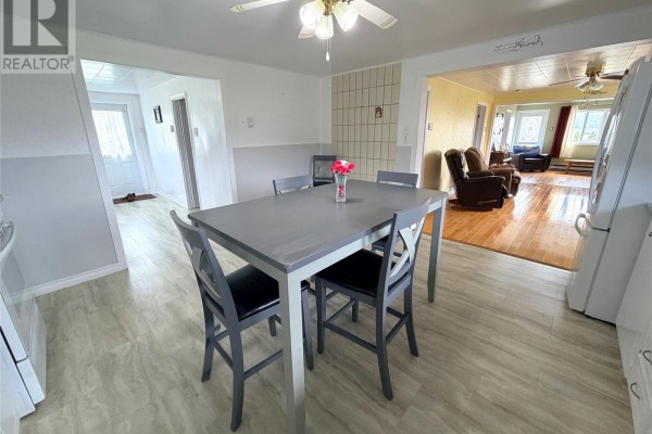 Dining area with a grey table and four chairs, next to a kitchen area and opening to a living room. - 242 Main Street, Norris Arm North