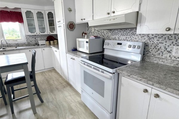 Close up of a white stove and kitchen cabinets with grey and white tile backsplash. - 242 Main Street, Norris Arm North