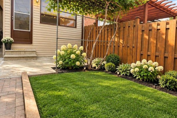 Lush green backyard with a wooden fence, flower beds, and a patio. - 242 Silverthorn Avenue, Toronto