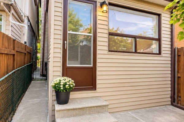 Side exterior view of a house with tan siding, a brown door, and a concrete walkway. - 242 Silverthorn Avenue, Toronto