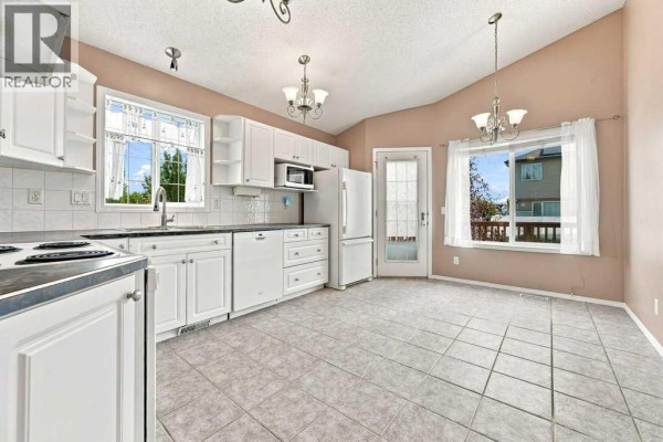 White kitchen with tile flooring, stainless steel appliances, and a door leading outside. - 242 Springs Place Se, Airdrie