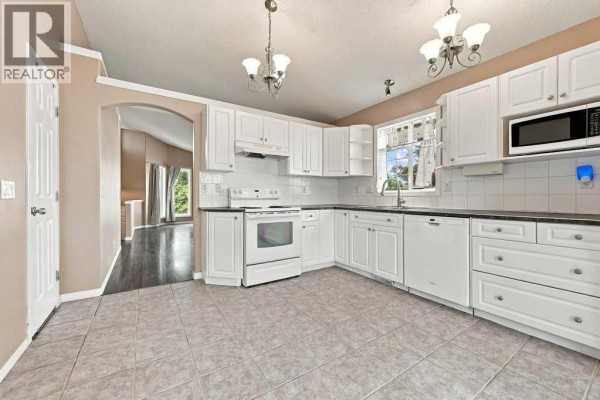 Spacious white kitchen with a large L-shaped counter, tile floor, and an archway view. - 242 Springs Place Se, Airdrie