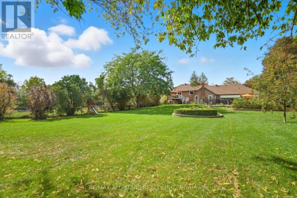 Large green lawn with mature trees and a view of the back of the house. - 242 Stephenson Point Road, Scugog