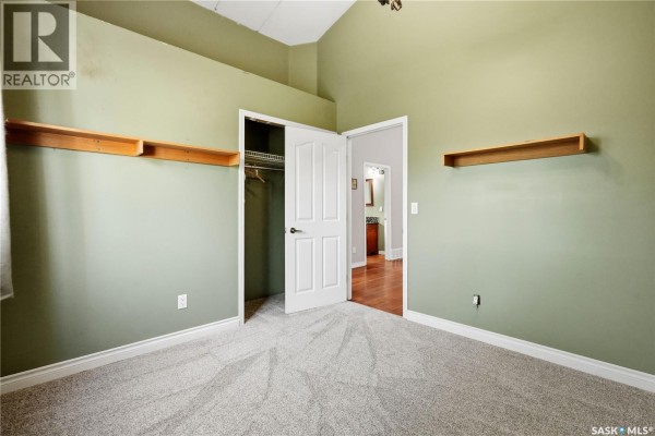 Bedroom with light green walls, plush grey carpet, open closet, and two wooden shelves. - 242 Woodlawn Avenue, Katepwa Beach