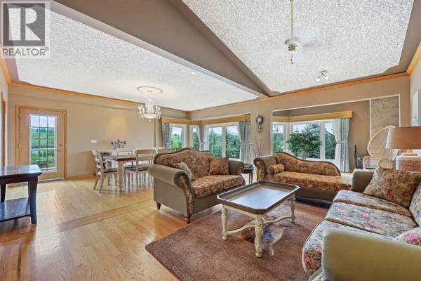 Living and dining area with large windows, floral sofas, a coffee table, dining table, and wood floors. - 242125 8 Street E, Rural Foothills County