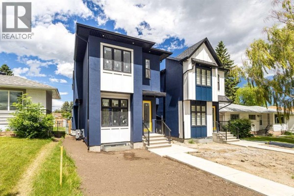 Side view of a modern blue and white duplex exterior with landscaped lawn and trees. - 2426 25 Avenue Nw, Calgary