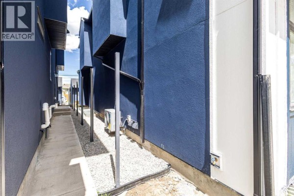 Narrow walkway between two modern blue duplex buildings with gravel landscaping. - 2426 25 Avenue Nw, Calgary