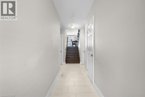 Interior hallway with light grey walls, tile floor, and staircase at end. - 243 Grey Silo Road Unit# 31, Waterloo