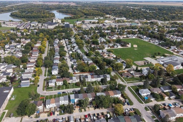 Aerial view of a residential neighborhood showing townhouses, streets, and a river in the distance. - 243 Houde Drive, Winnipeg
