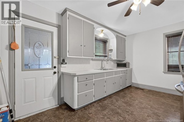 Kitchen showing a sink, grey cabinets, a glass-paned door, and blinds on window. - 243 Mill Road, Moncton