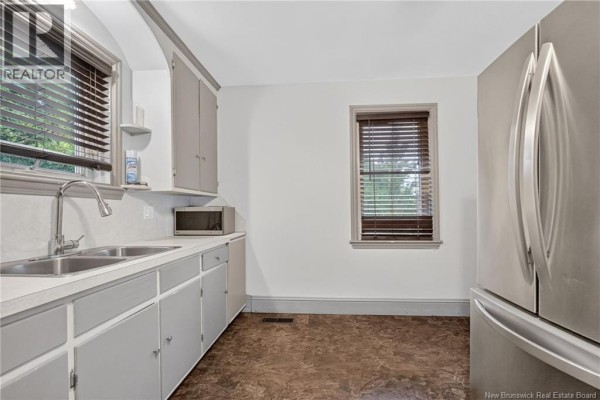 Kitchen with sink, grey cabinets, and stainless steel refrigerator against a white wall. - 243 Mill Road, Moncton