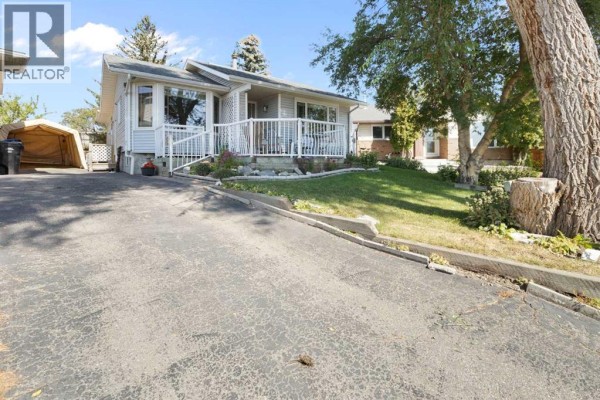Low angle view of a light blue house with a driveway and mature tree on the right. - 243 Radcliffe Place Se, Calgary