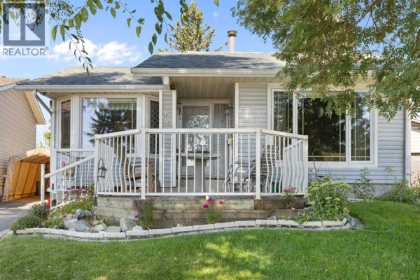 Close-up of the front porch with white railing, patio chairs, and flower beds. - 243 Radcliffe Place Se, Calgary