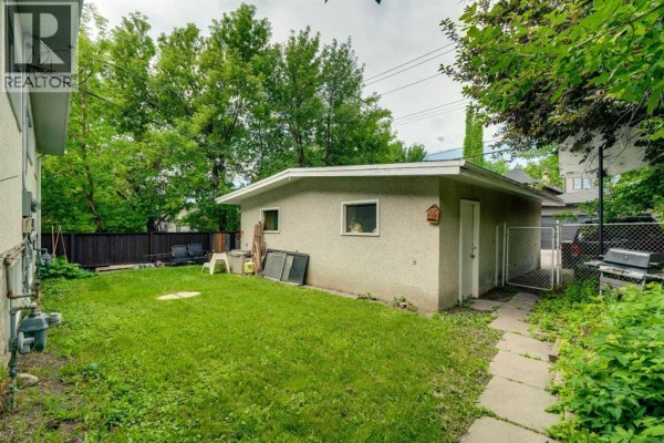 A single-car garage with stucco siding and a fenced yard, including a barbecue and patio chairs. - 2431 & 2429 26 Street Sw, Calgary
