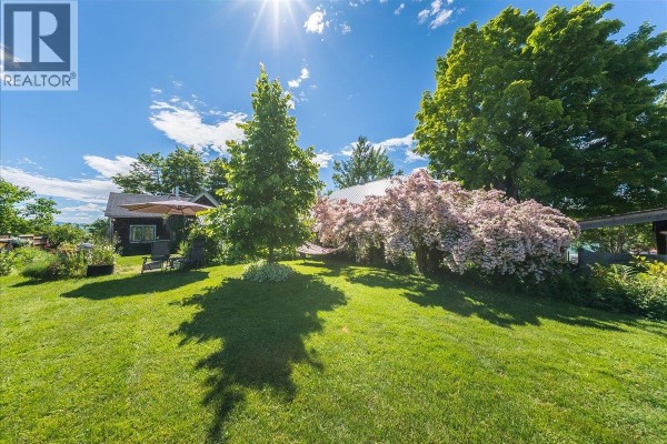 A spacious green lawn with trees, a flowering tree, and outdoor seating area. - 2433 First Avenue, Rossland