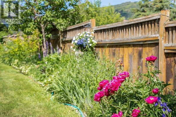 A wooden fence borders a garden with vibrant pink peonies and green foliage. - 2433 First Avenue, Rossland