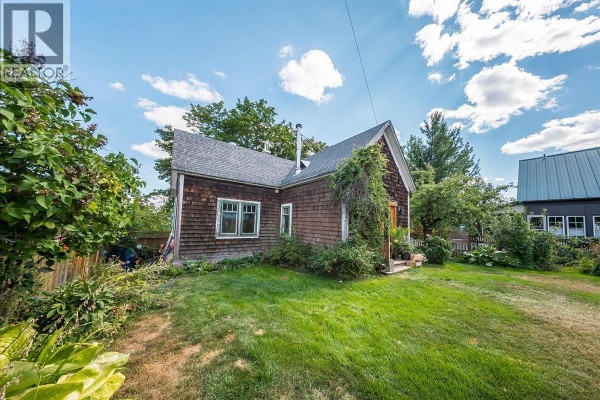 Side view of a wooden shake house with green landscaping and a pathway. - 2433 First Avenue, Rossland
