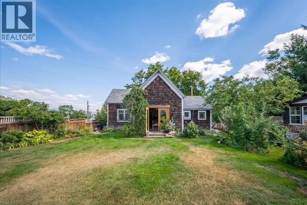 Front view of a small house with a wooden shake exterior and a large green lawn. - 2433 First Avenue, Rossland