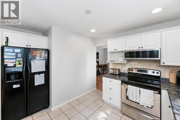 Kitchen with white cabinets, stainless steel stove, black refrigerator, and tiled floor. - 2437 Benko Rd, Mill Bay