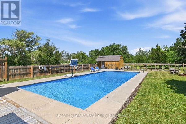 Rectangular swimming pool with concrete surround, wooden fence, and a small shed. - 2439 Miller Road, Port Colborne