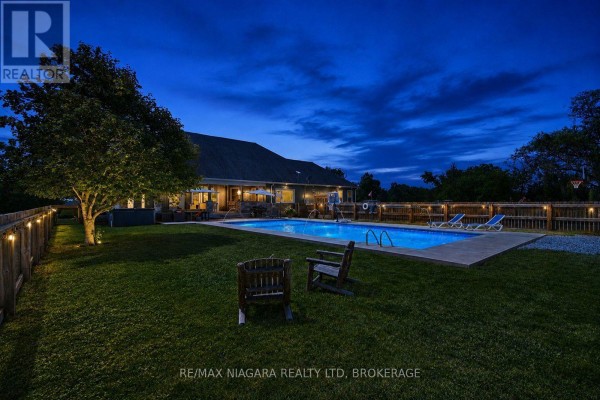 Backyard at night with a swimming pool, chairs, and outdoor lighting. - 2439 Miller Road, Port Colborne