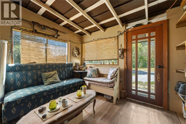 Sunroom with a blue patterned sofa, bench seating, and bamboo blinds on the window. - 244 Mabel Lake Road, Lumby