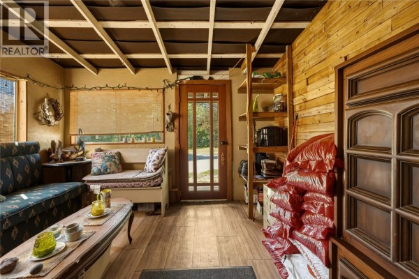 Interior room with wood-paneled walls, a sofa, bench, shelves of items, and a wooden door. - 244 Mabel Lake Road, Lumby