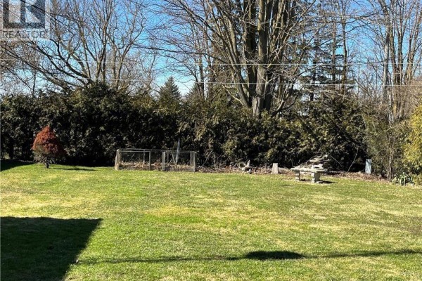Backyard view of a residential property with mature trees, a chicken coop, and a stone bench. - 244 Main Street, Atwood