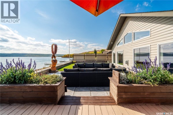 Lakefront backyard patio with sectional sofa, planter boxes with purple flowers, and wooden deck. - 244 Moose Road, Crooked Lake